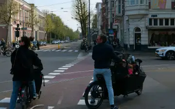 Padres con niños en bicicletas de carga en un cruce con carril bici rojo de la Plantage Middenlaan, en Ámsterdam