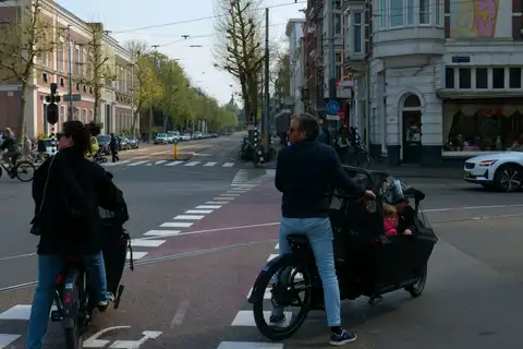 Padres con niños en bicicletas de carga en un cruce con carril bici rojo de la Plantage Middenlaan, en Ámsterdam