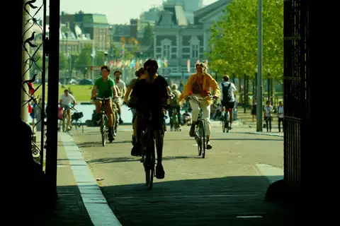 Ciclistas cruzando el pasaje bajo el Rijksmuseum de Ámsterdam, a contraluz, con la explanada y árboles al fondo
