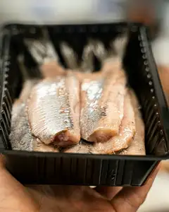 Filetes de arenque holandés crudo (Hollandse Nieuwe) en una bandeja negra sostenida con una mano