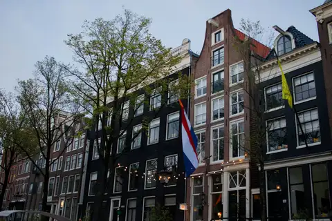 Bandera roja, blanca y azul de los Países Bajos colgada de la fachada de ladrillo de una casa de canal de Ámsterdam