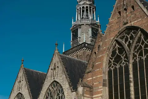 Torre y ventanales góticos de la Oude Kerk de Ámsterdam, de ladrillo y piedra, bajo un cielo azul despejado