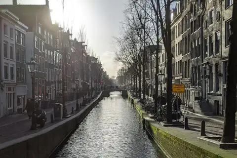Canal Oudezijds Achterburgwal de día con casas altas de ladrillo, bicicletas aparcadas junto al agua y un puente al fondo