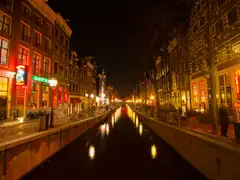 Canal del Barrio Rojo de Ámsterdam de noche, con casas de ladrillo iluminadas en rojo y reflejos de luces en el agua oscura