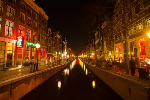 Canal del Barrio Rojo de Ámsterdam de noche, con casas de ladrillo iluminadas en rojo y reflejos de luces en el agua oscura