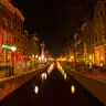 Canal del Barrio Rojo de Ámsterdam de noche, con casas de ladrillo iluminadas en rojo y reflejos de luces en el agua oscura