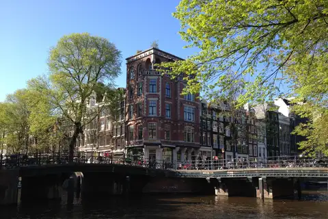 Casas altas de ladrillo junto al canal Herengracht de Ámsterdam, con un puente con bicicletas y árboles en primavera