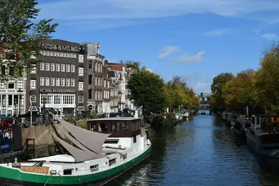 Canal del Jordaan en Ámsterdam con casas de ladrillo, casas flotantes amarradas y árboles de otoño bajo un cielo azul
