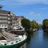 Canal del Jordaan en Ámsterdam con casas de ladrillo, casas flotantes amarradas y árboles de otoño bajo un cielo azul