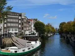 Canal del Jordaan en Ámsterdam con casas de ladrillo, casas flotantes amarradas y árboles de otoño bajo un cielo azul