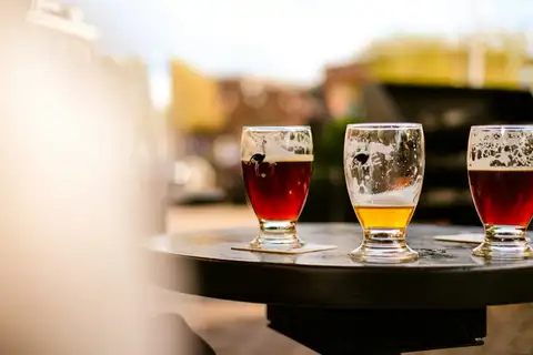 Tres vasos de cerveza artesana, dos rojizos y uno dorado, sobre una mesa exterior de la cervecería Brouwerij ’t IJ de Ámsterdam