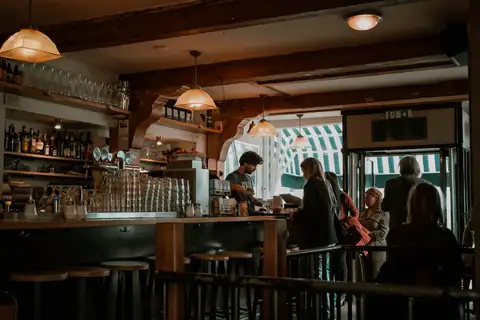 Interior de un café tradicional de Ámsterdam con vigas de madera oscura, barra con vasos y luces colgantes, y clientes al fondo