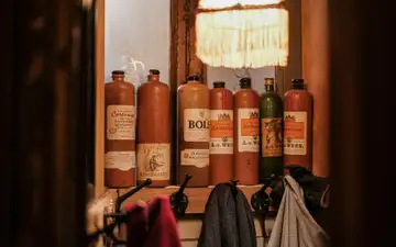 Botellas tradicionales de gres de jenever con etiquetas antiguas alineadas en una repisa de madera de un café de Ámsterdam