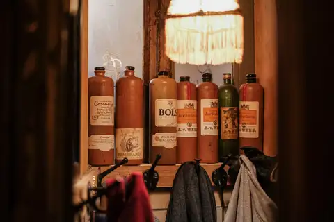 Botellas tradicionales de gres de jenever con etiquetas antiguas alineadas en una repisa de madera de un café de Ámsterdam