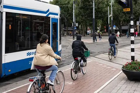 Ciclistas por un carril bici de ladrillo rojo junto a un tranvía azul y blanco en un cruce del centro de Ámsterdam