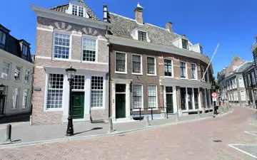 Fachadas de ladrillo con grandes ventanas blancas de cristales y puertas verdes en una calle empedrada del centro de Utrecht