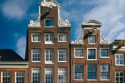 Fachadas de ladrillo con aguilones de volutas blancas y ventanas de guillotina de casas de canal típicas de Ámsterdam bajo un cielo azul