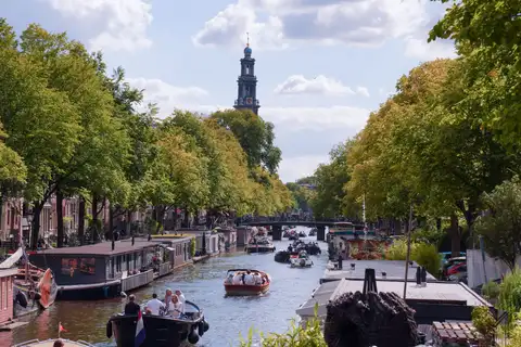 Torre de la Westerkerk sobre el canal Prinsengracht, con barcas navegando entre casas flotantes y árboles frondosos en Ámsterdam
