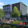 Edificio de ladrillo y cristal de la Casa de Ana Frank junto al canal Prinsengracht, con visitantes haciendo cola y flores en primer plano