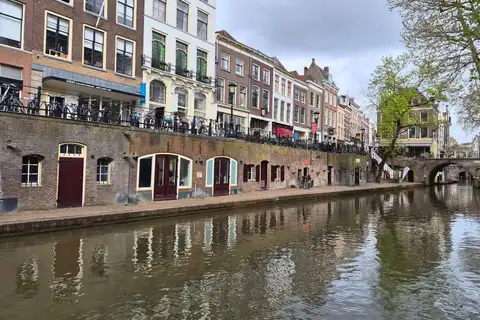 Canal Oudegracht de Utrecht con muelles de ladrillo a ras de agua, bodegas con puertas y fachadas antiguas, y un puente al fondo