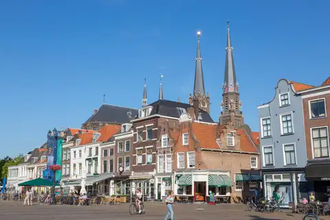 Plaza del centro de Delft con fachadas de ladrillo y de aguilones, terrazas con bicicletas y torres de iglesia bajo un cielo azul