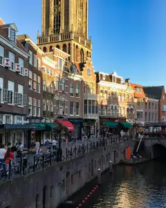 Canal del casco antiguo de Utrecht con ciclistas y peatones en el muelle, fachadas de ladrillo y la torre del Dom al fondo