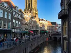 Canal del casco antiguo de Utrecht con ciclistas y peatones en el muelle, fachadas de ladrillo y la torre del Dom al fondo