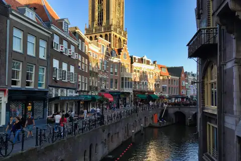 Canal del casco antiguo de Utrecht con ciclistas y peatones en el muelle, fachadas de ladrillo y la torre del Dom al fondo
