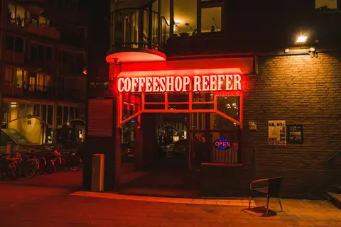 Entrada de un coffeeshop de Ámsterdam de noche, con luz roja de neón sobre la puerta, cartel de abierto y bicicletas aparcadas a la izquierda
