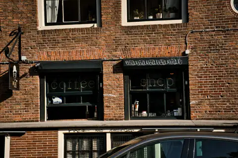Fachada de ladrillo rojo de un coffeeshop con rótulo «coffee shop» en las ventanas, en un edificio histórico de Ámsterdam