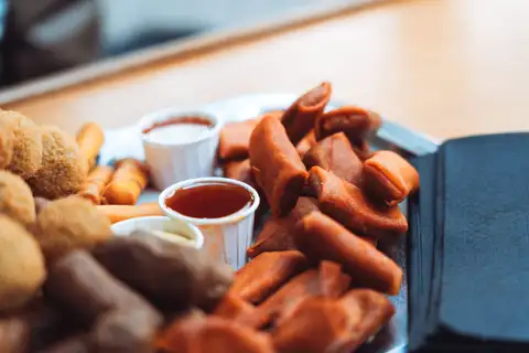 Bandeja de picoteo holandés con bitterballen, rollitos fritos y salsas en vasitos de papel sobre una mesa de madera en un café de Ámsterdam