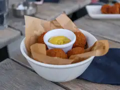 Cuenco blanco con bitterballen dorados y un pequeño recipiente de mostaza amarilla sobre una mesa de madera en una terraza