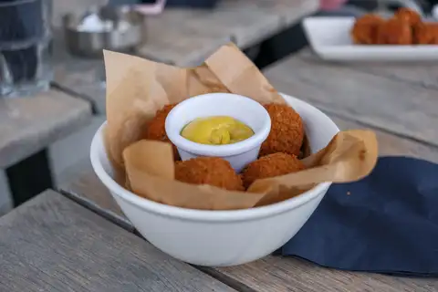 Cuenco blanco con bitterballen dorados y un pequeño recipiente de mostaza amarilla sobre una mesa de madera en una terraza