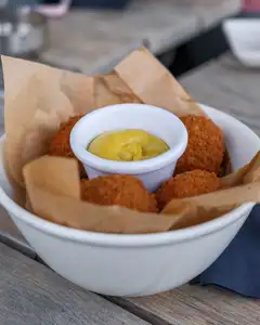 Cuenco blanco con bitterballen dorados y un pequeño recipiente de mostaza amarilla sobre una mesa de madera en una terraza
