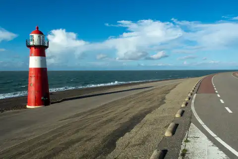 Faro rojo y blanco junto a una carretera sobre el dique de Westkapelle, en Zelanda, con el mar del Norte a un lado y cielo azul