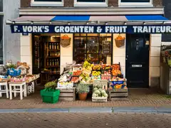 Fachada de una frutería y verdulería de Ámsterdam con cajas de fruta, alcachofas y cestas de la compra verdes en la acera de ladrillo