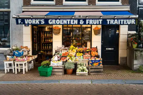 Fachada de una frutería y verdulería de Ámsterdam con cajas de fruta, alcachofas y cestas de la compra verdes en la acera de ladrillo