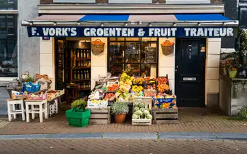 Fachada de una frutería y verdulería de Ámsterdam con cajas de fruta, alcachofas y cestas de la compra verdes en la acera de ladrillo