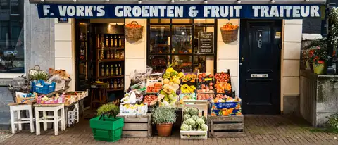 Fachada de una frutería y verdulería de Ámsterdam con cajas de fruta, alcachofas y cestas de la compra verdes en la acera de ladrillo