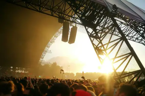 Público de espaldas ante un gran escenario de estructura metálica en un festival de música al aire libre en Holanda, con el sol poniente al fondo
