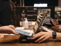 Manos acercando un teléfono móvil al datáfono contactless sobre el mostrador de madera de un café
