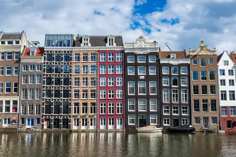 Fila de estrechas casas del canal de Ámsterdam, de ladrillo y de colores, reflejadas en el agua bajo un cielo con nubes