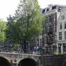 Casas de ladrillo con frontones y un puente de piedra con bicicletas aparcadas junto a un canal de Ámsterdam, en un día soleado