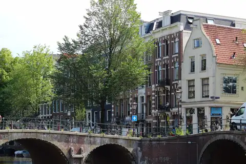 Casas de ladrillo con frontones y un puente de piedra con bicicletas aparcadas junto a un canal de Ámsterdam, en un día soleado