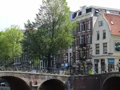 Casas de ladrillo con frontones y un puente de piedra con bicicletas aparcadas junto a un canal de Ámsterdam, en un día soleado
