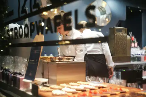 Dos dependientes con uniforme blanco trabajan tras el mostrador de una tienda de stroopwafels en Ámsterdam, con gofres decorados en primer plano