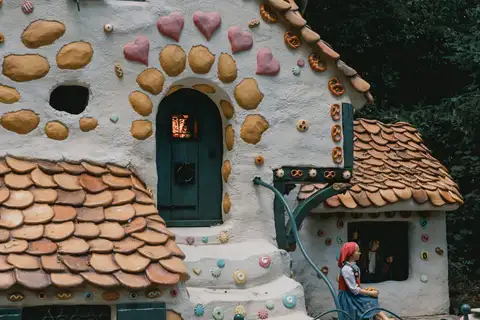 Casa de la bruja de pan de jengibre con corazones, galletas y pretzels en la fachada, y una figura de niña con pañuelo rojo