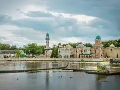 Edificios de estilo árabe con cúpulas turquesa y minarete junto al estanque del parque Efteling, con una rana gigante en el agua
