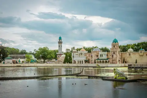 Edificios de estilo árabe con cúpulas turquesa y minarete junto al estanque del parque Efteling, con una rana gigante en el agua