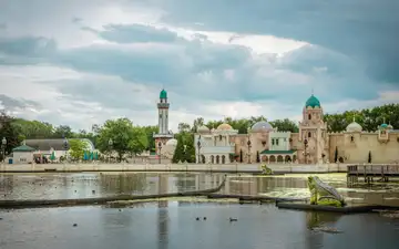 Edificios de estilo árabe con cúpulas turquesa y minarete junto al estanque del parque Efteling, con una rana gigante en el agua